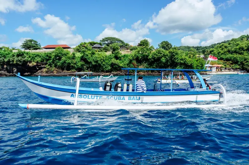 Un bateau bleu et blanc navigue sur une mer turquoise sous un ciel nuageux.