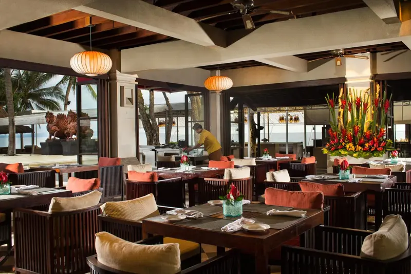 Une salle à manger lumineuse avec des tables dressées et une vue sur la plage.