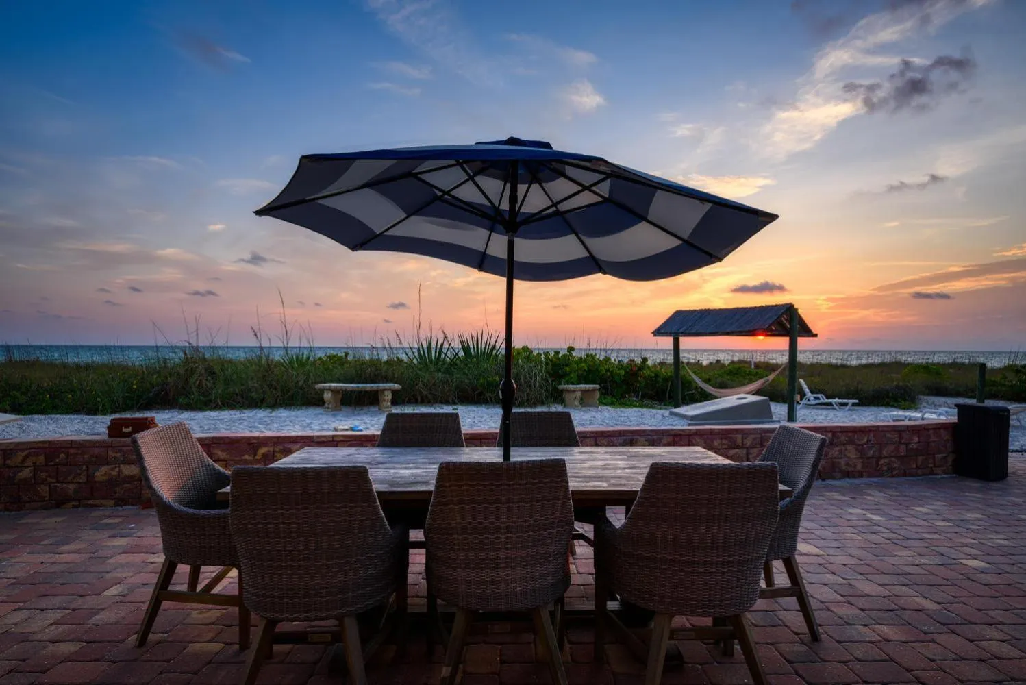 Table et chaises sur une terrasse en pavés face à la mer au coucher du soleil.