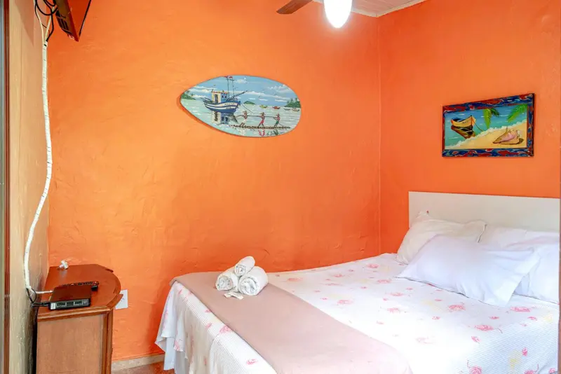 Une chambre lumineuse aux murs orange avec un lit recouvert de draps blancs.