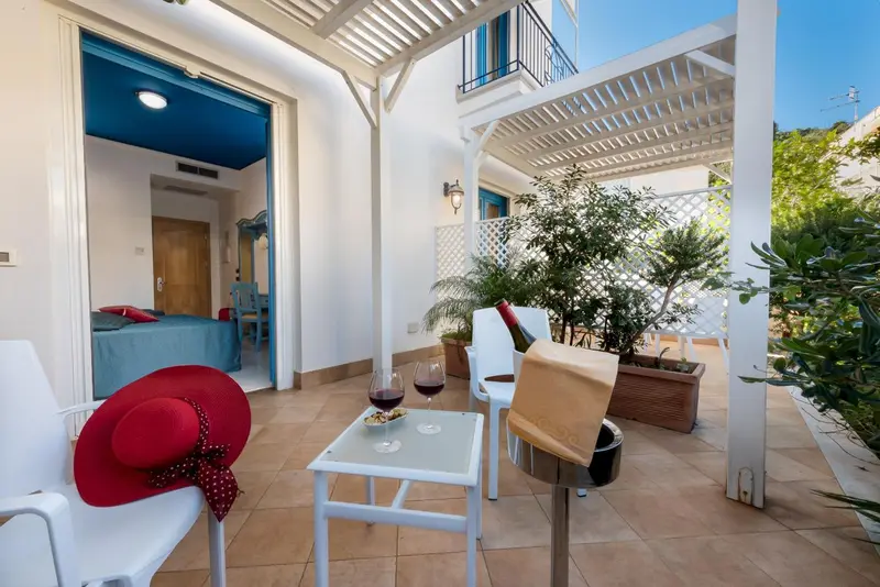 Une table basse avec des verres de vin et des chapeaux est placée sur une terrasse carrelée.