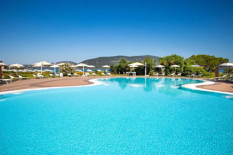 Piscine turquoise aux formes sinueuses avec transats et parasols blancs.