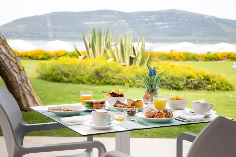Une table de petit-déjeuner est dressée devant une vue sur la mer et la végétation.