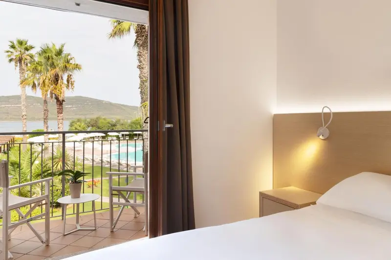 Une chambre lumineuse s'ouvre sur une terrasse avec vue sur la végétation et la mer.