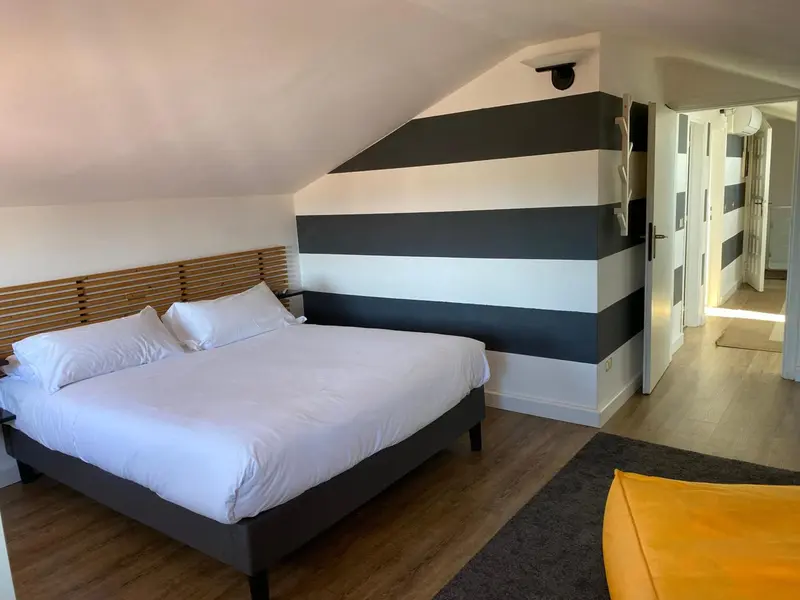 Une chambre lumineuse avec un lit double et un mur rayé.