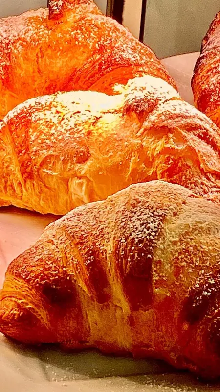 Des viennoiseries dorées recouvertes de sucre glace sont présentées en gros plan.