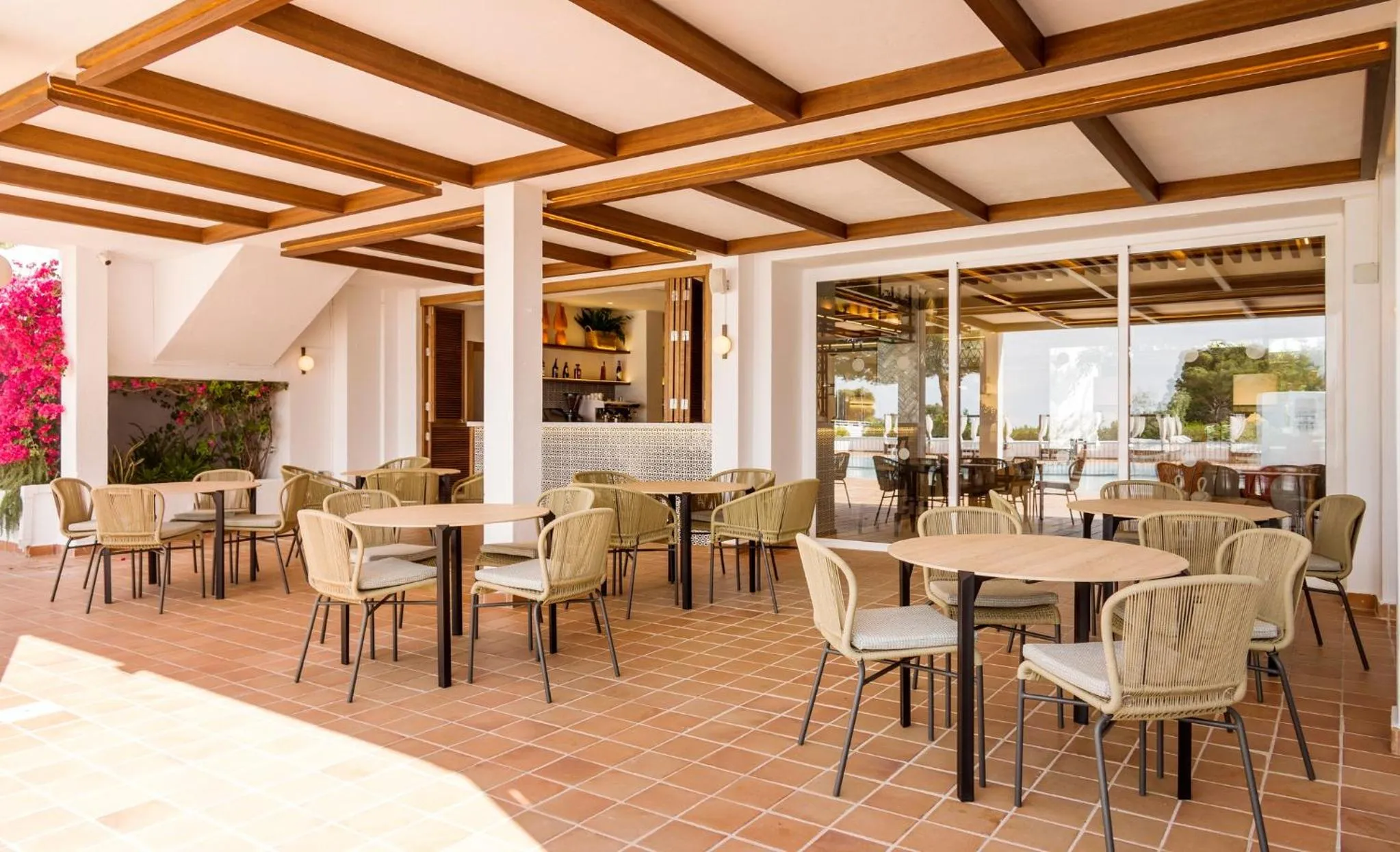 Terrasse ombragée avec tables et chaises, donnant sur un espace bar et une piscine.