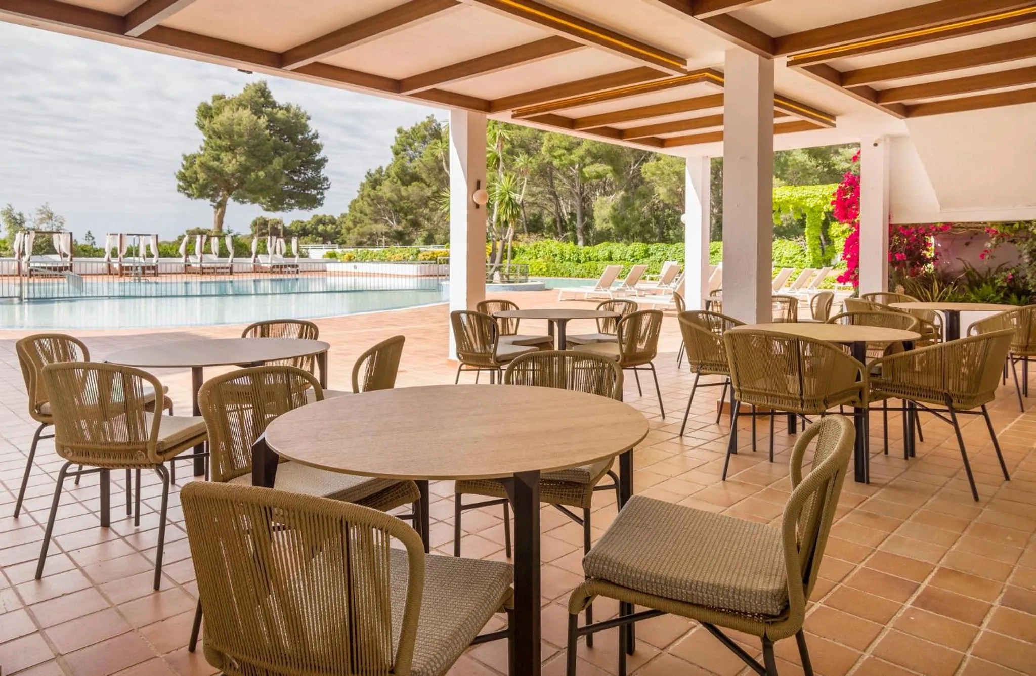 Terrasse ombragée avec tables et chaises près d'une piscine.