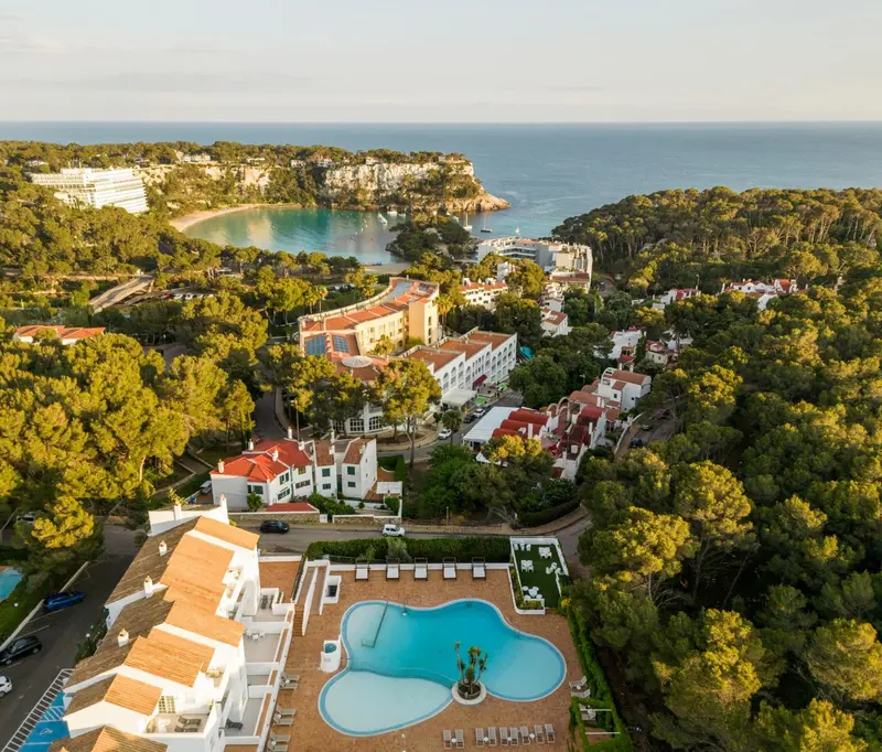 Vue aérienne d'un complexe hôtelier avec piscine et végétation luxuriante surplombant une crique.