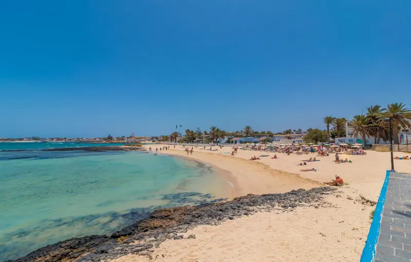 Une plage de sable fin bordée d'une eau turquoise sous un ciel bleu dégagé.