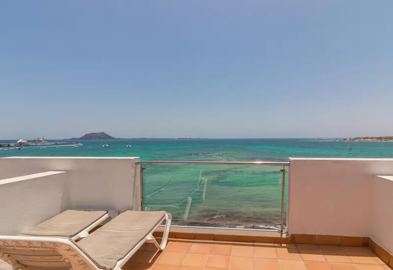 Terrasse avec transats donnant sur une mer turquoise et une côte rocheuse.