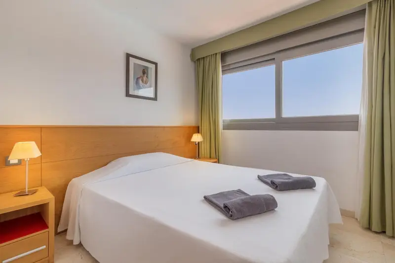Une chambre lumineuse avec un grand lit blanc et deux tables de chevet.