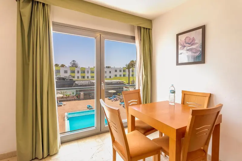 Une table et des chaises sont placées devant de grandes baies vitrées donnant sur une piscine.