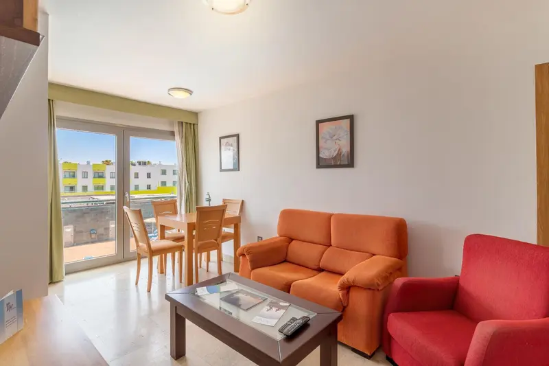Un salon lumineux avec canapé orange et table à manger près d'une baie vitrée.