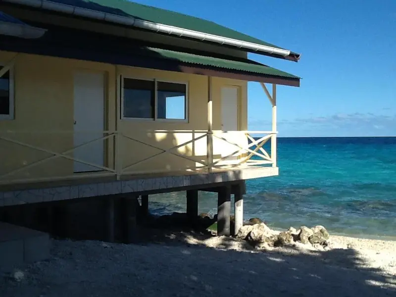 Une cabane jaune sur pilotis surplombe une plage de sable blanc et une mer turquoise.