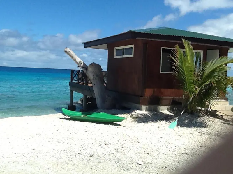 Une cabane en bois sur pilotis borde une plage de sable blanc face à une mer turquoise.