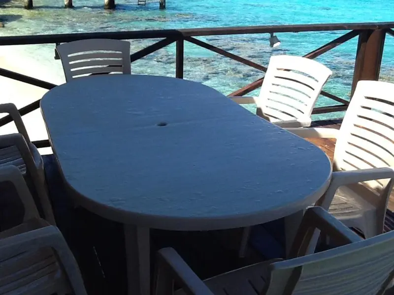 Table et chaises en plastique sur une terrasse en bois avec vue sur la mer.