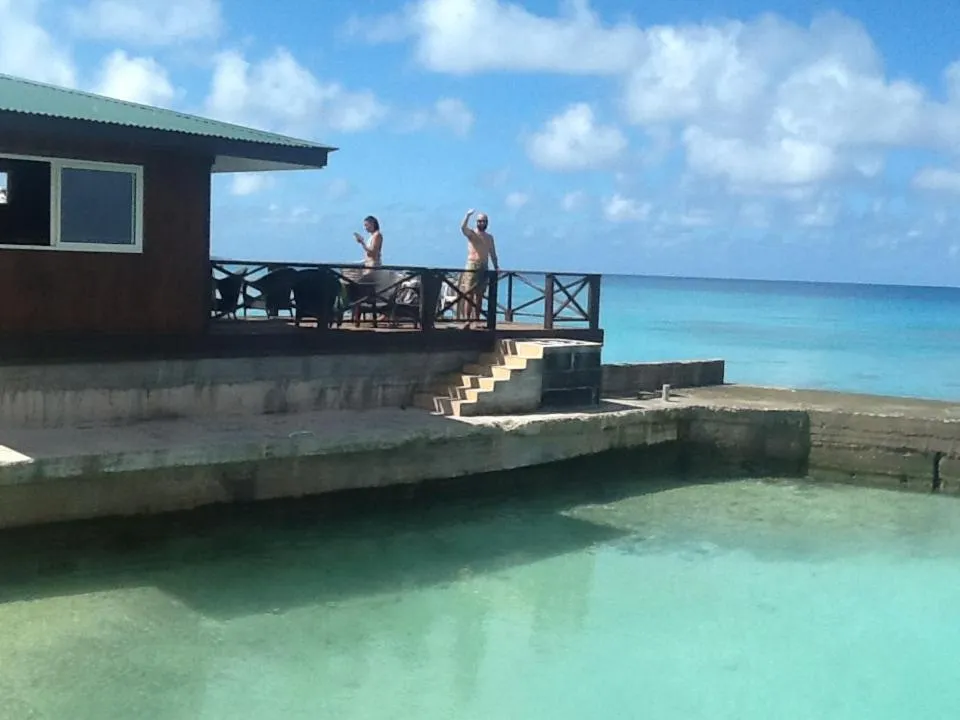 Deux personnes se tiennent sur une terrasse en bois surplombant une eau turquoise.
