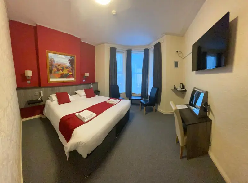 Chambre lumineuse avec un grand lit et un bureau.