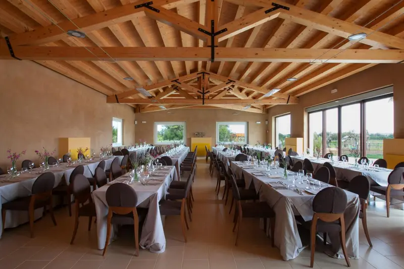 Une grande salle lumineuse est mise en scène pour un repas avec des tables dressées et des chaises.