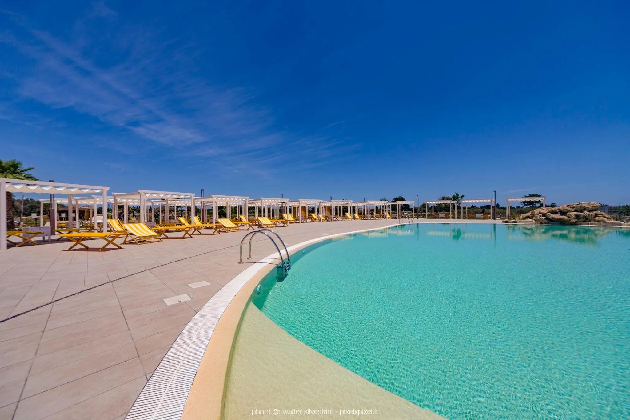 Une piscine rectangulaire bordée d'une terrasse avec des transats.
