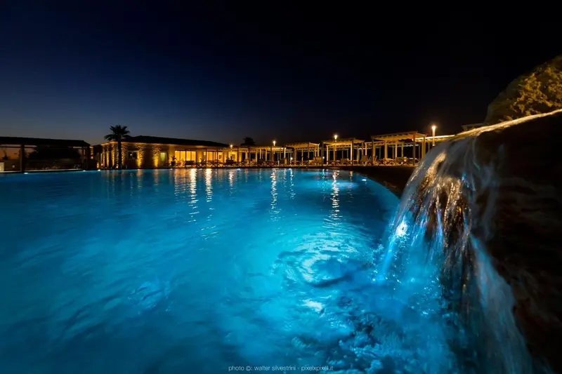 Une cascade artificielle se jette dans une piscine illuminée la nuit.