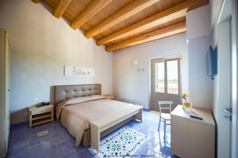 Chambre lumineuse avec un grand lit et une porte-fenêtre donnant sur l'extérieur.