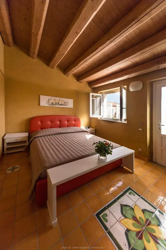 Une chambre à coucher lumineuse avec un lit recouvert d'une courtepointe et un sol carrelé.