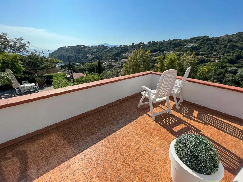 Terrasse carrelée avec mobilier d'extérieur et vue sur la végétation.