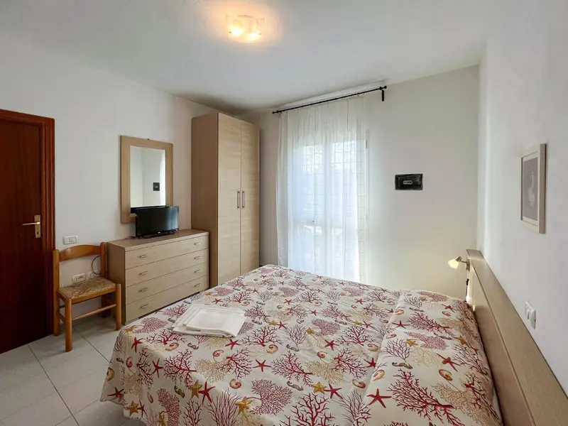 Une chambre lumineuse avec un lit recouvert d'une couette à motifs et un meuble télé.