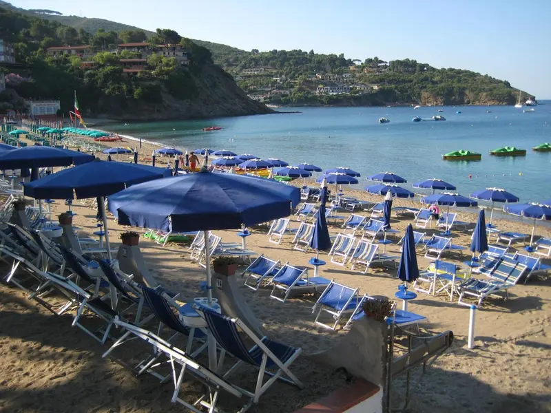 Une plage ensoleillée avec des transats bleus et des parasols.