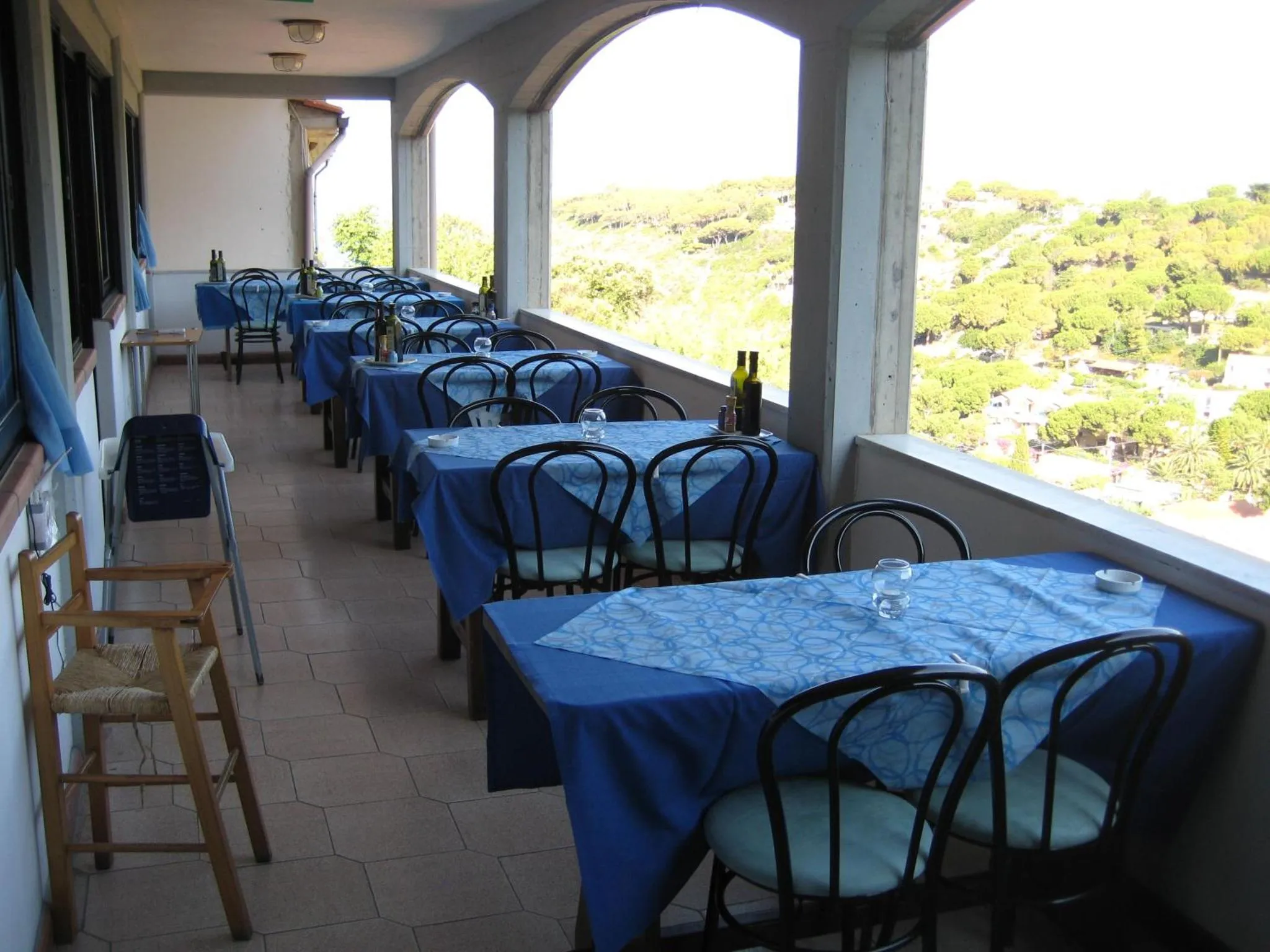 Terrasse ombragée avec tables et chaises donnant sur un paysage vallonné.