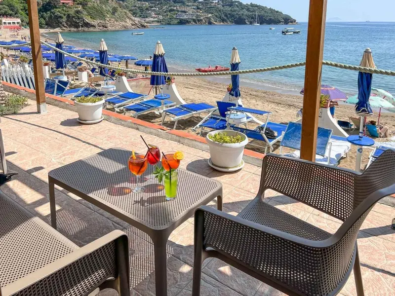 Tables et chaises sur une terrasse ensoleillée avec vue sur la plage et la mer.