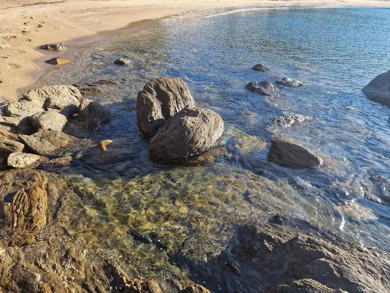 Des rochers émergent dans une eau turquoise le long d'une plage de sable.