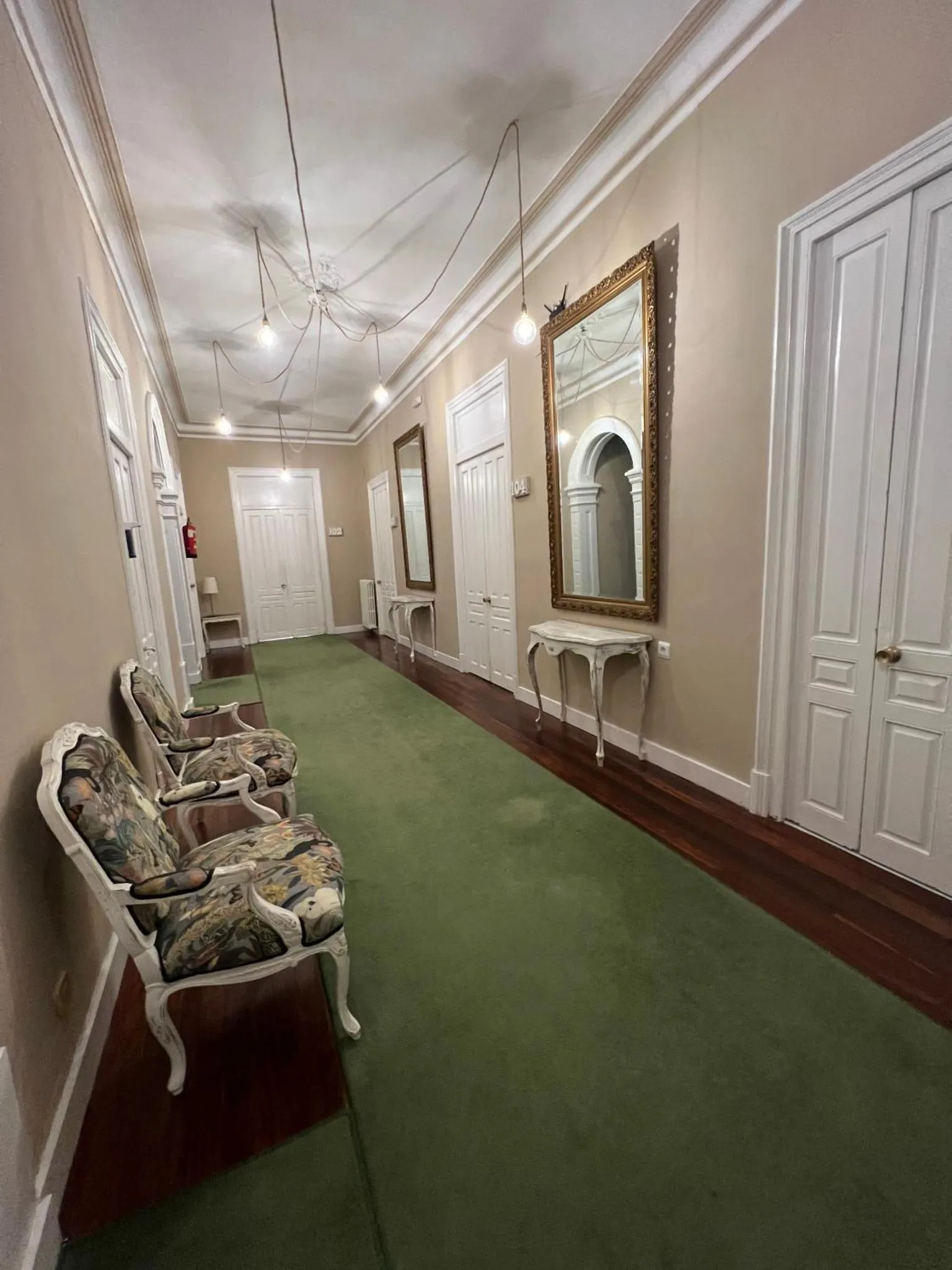 Un long couloir d'hôtel avec des portes blanches de chaque côté et un tapis vert.