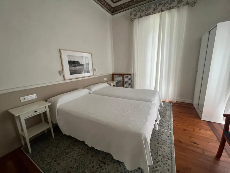 Une chambre lumineuse avec un lit recouvert d'une couverture blanche et un parquet en bois.