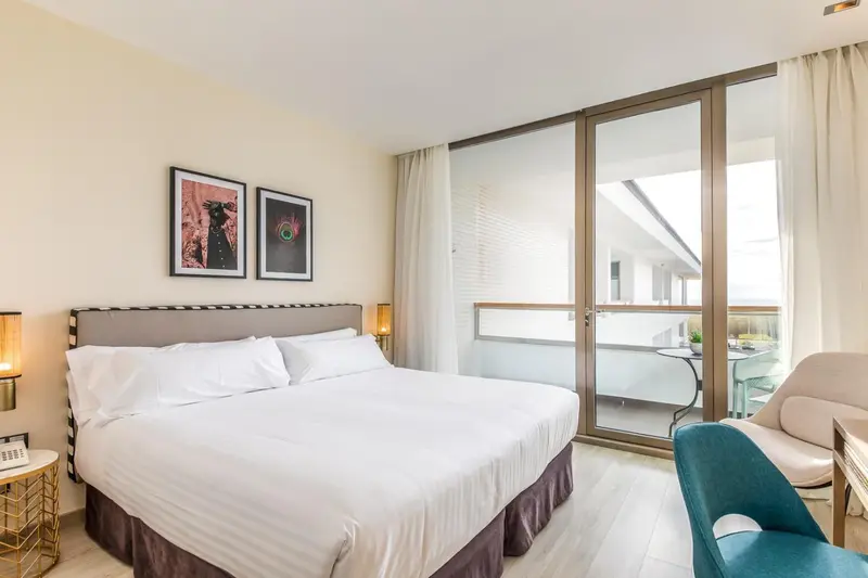 Une chambre lumineuse avec un grand lit et un accès à un balcon.