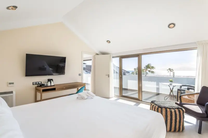 Une chambre lumineuse avec un lit blanc et un accès à une terrasse.