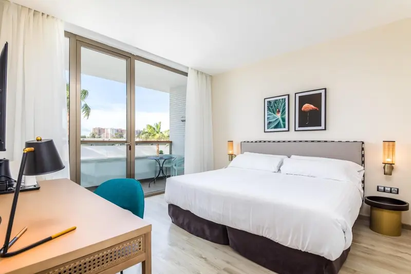 Une chambre lumineuse avec un grand lit et un balcon donnant sur la végétation.