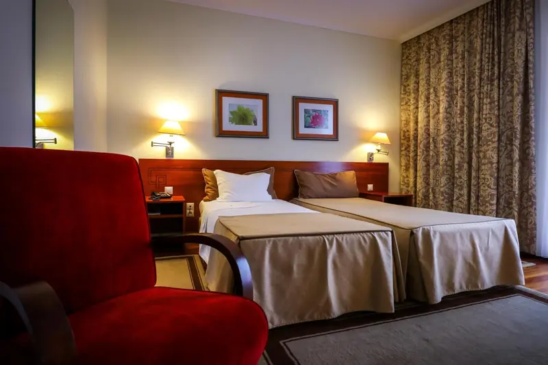 Une chambre d'hôtel lumineuse avec un lit double et un fauteuil rouge.
