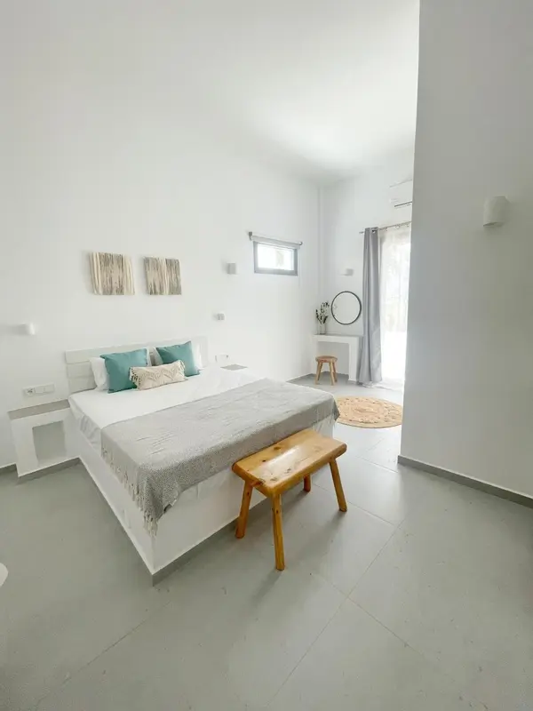 Chambre lumineuse avec un lit recouvert d'une couverture grise et de coussins turquoise.