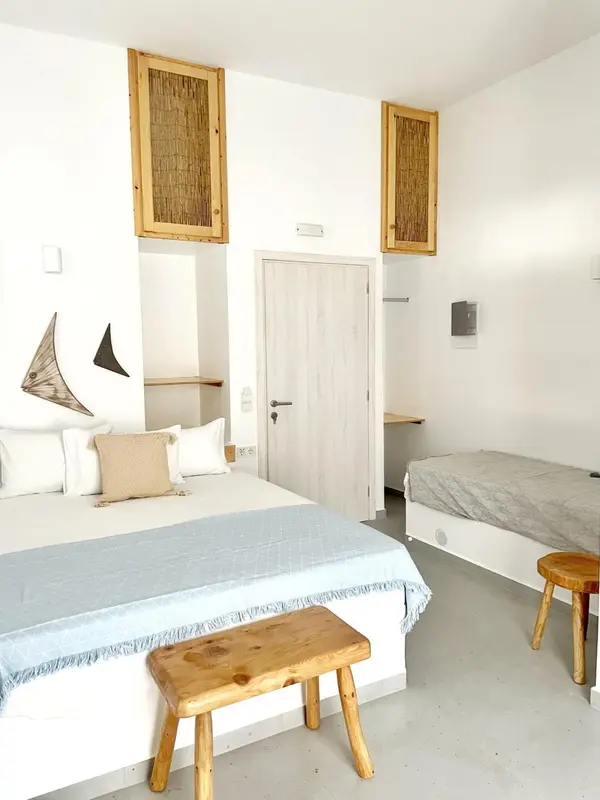 Une chambre lumineuse avec un lit recouvert d'une couverture bleue et un petit banc en bois.