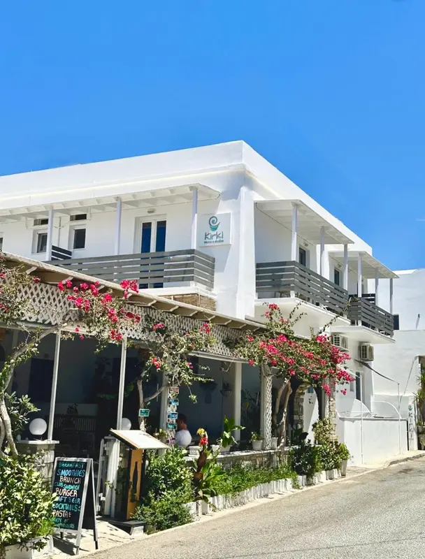 Bâtiment blanc à deux étages avec des balcons fleuris et une terrasse ombragée.