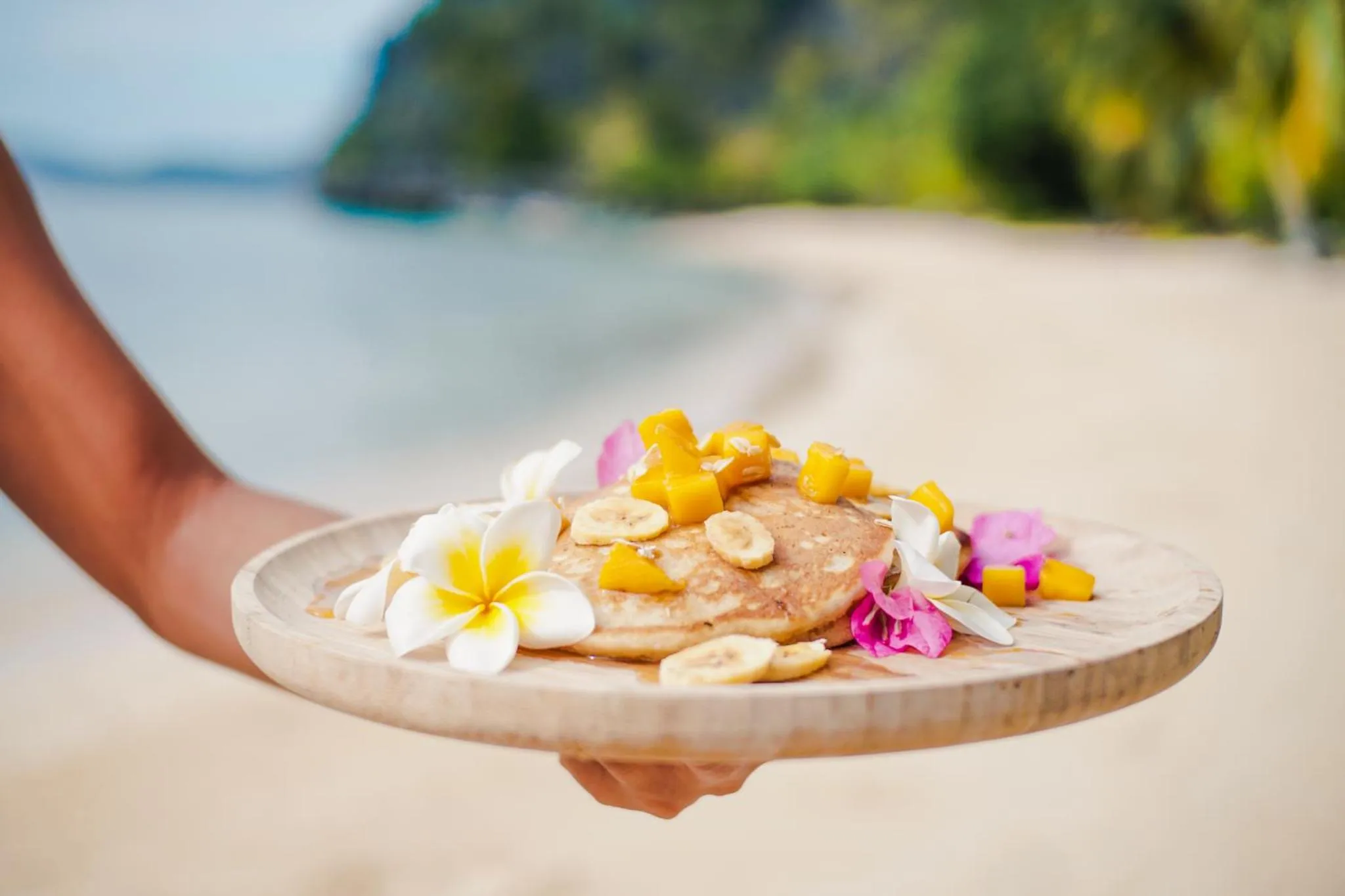 Une assiette de crêpes aux fruits est présentée sur une plage de sable blanc.