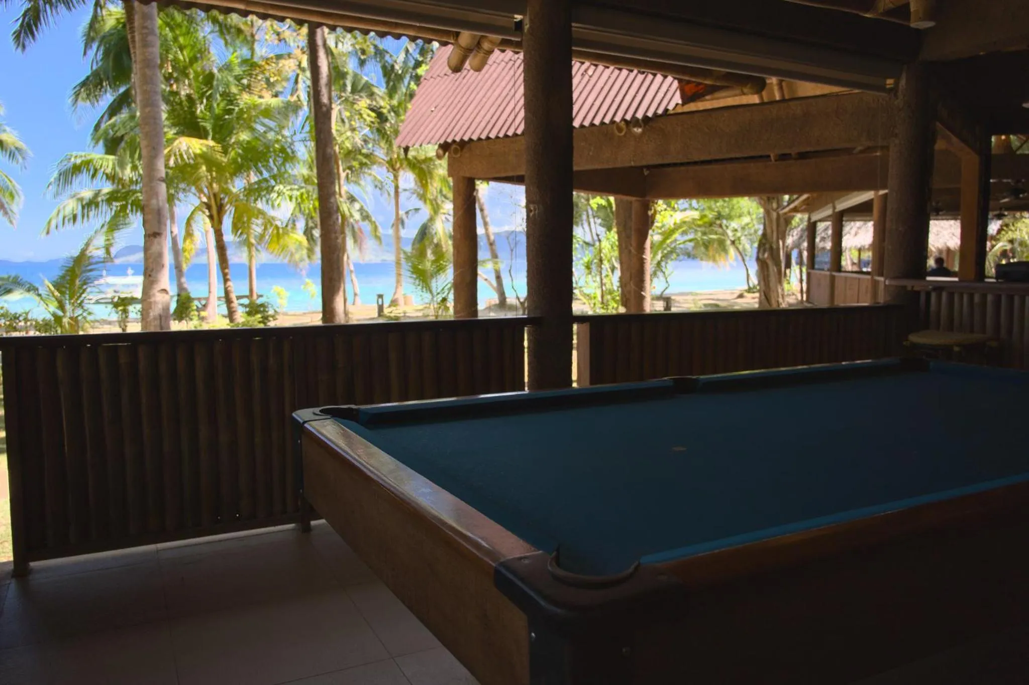 Une table de billard se trouve sur une terrasse ombragée avec vue sur la mer et la végétation.