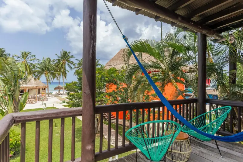 Terrasse en bois avec hamac et mobilier d'extérieur donnant sur une plage tropicale.