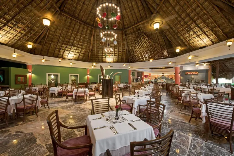 Une salle de restaurant lumineuse avec des tables dressées et un décor tropical.