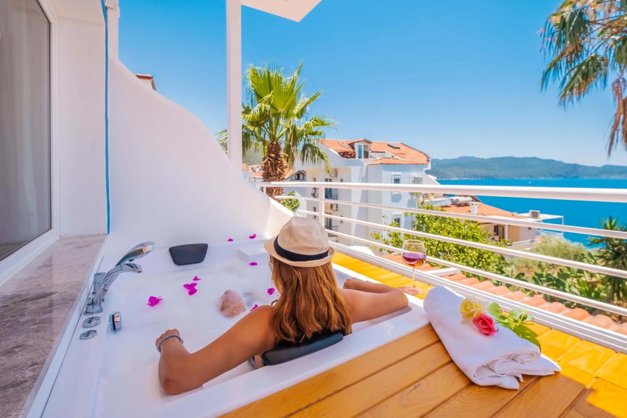 Une personne se détend dans un jacuzzi sur une terrasse ensoleillée avec vue sur la mer.