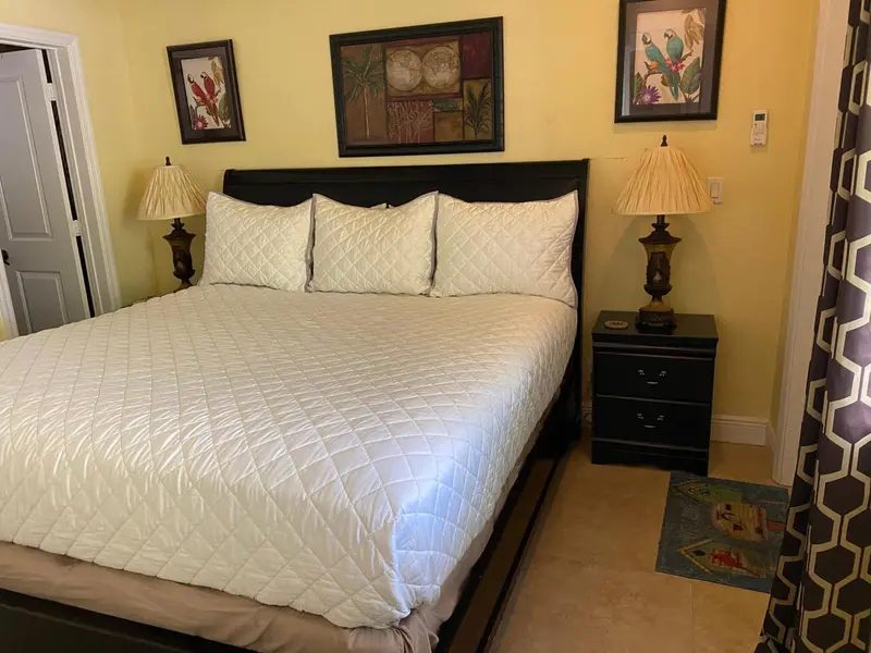 Une chambre lumineuse avec un grand lit recouvert d'une courtepointe blanche et de coussins.