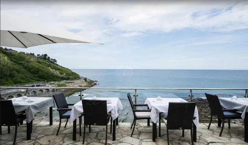 Terrasse avec tables et chaises donnant sur la mer et la côte.